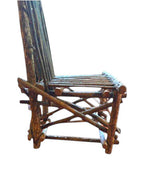 Vintage, handmade rustic twig chair in a low right profile view featuring tall, branching backrest, slatted branch seat, and cross-braced legs. Made from raw branches with unpeeled bark. Sold vintage as-is in very good condition.
