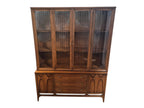 Mid Century Modern Broyhill Brasilia walnut breakfront China cabinet in a front view. Features the Brasilia collection's catseye sweeping arches and tapered legs, with brass hardware and glass display doors. Vintage as-is, gently refreshed, including credenza base with three drawers and two doors and top display deck with two doors.