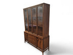 Mid Century Modern Broyhill Brasilia walnut breakfront China cabinet in a left-front view. Features the Brasilia collection's catseye sweeping arches and tapered legs, with brass hardware and glass display doors. Vintage as-is, gently refreshed, including credenza base with three drawers and two doors and top display deck with two doors.