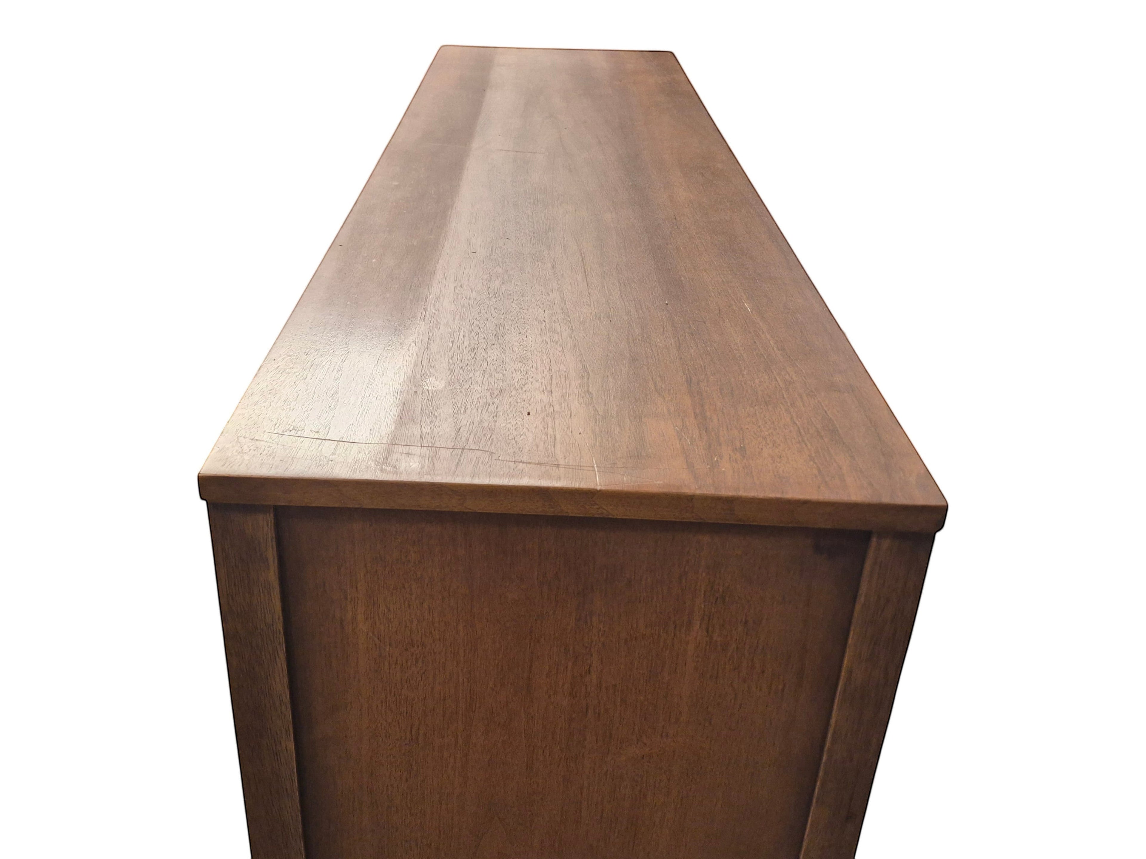 Mid Century Modern Broyhill Brasilia walnut base credenza, the lower half of the breakfront China cabinet set, in a left profile view. Features the Brasilia collection's catseye sweeping arches, tapered legs, and brass hardware. Vintage as-is, gently refreshed, as a pair with top display deck.