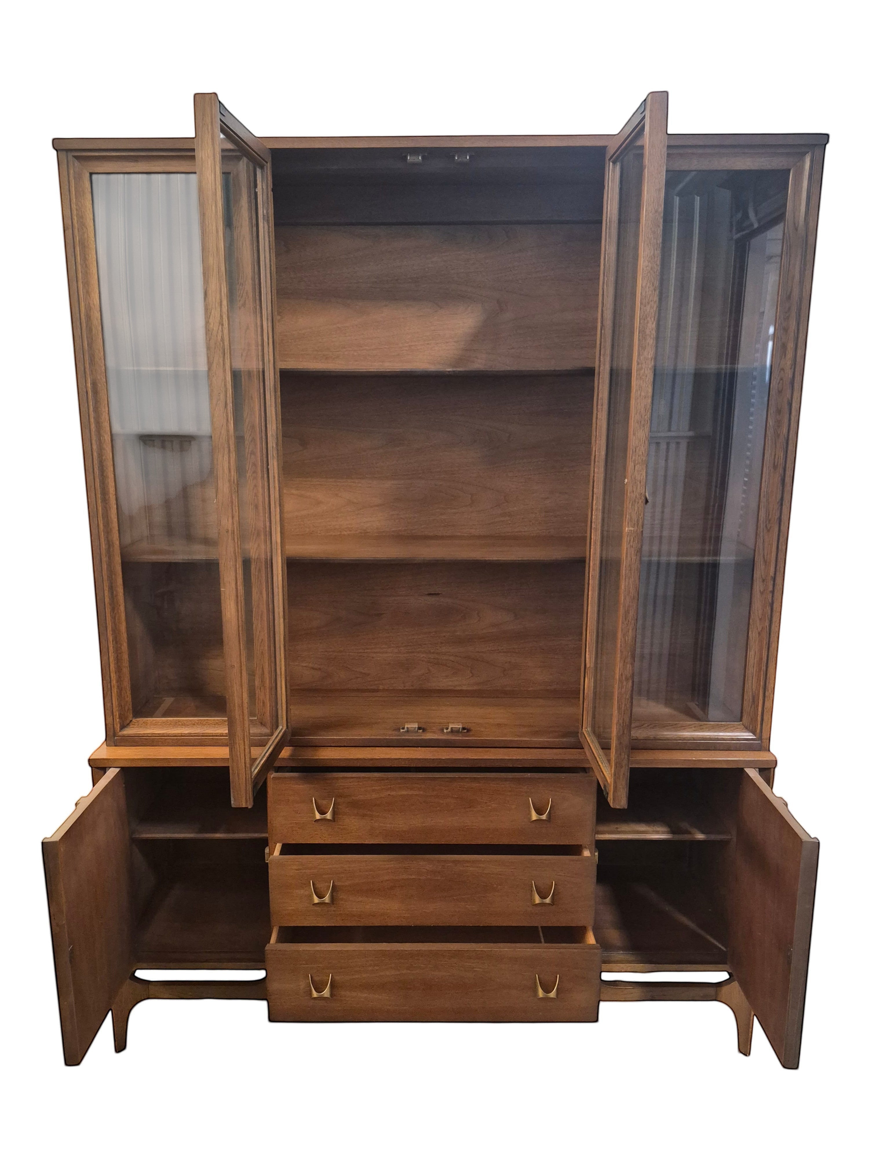 Mid Century Modern Broyhill Brasilia walnut breakfront China cabinet in a front view, with open doors and drawers. Features the Brasilia collection's catseye sweeping arches and tapered legs, with brass hardware and glass display doors. Vintage as-is, gently refreshed, including credenza base with three drawers and two doors and top display deck with two doors.