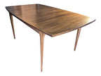 Mid Century Modern Broyhill Brasilia walnut dining table in a front-right angle view. Features the Brasilia collection's signature tapered legs and bow-sided rectangle table top. Sold as-is, gently refreshed, including three interior leaves.