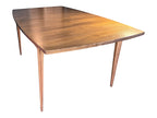 Mid Century Modern Broyhill Brasilia walnut dining table in a front-right angle view. Features the Brasilia collection's signature tapered legs and bow-sided rectangle table top. Vintage as-is, gently refreshed, including three interior leaves.