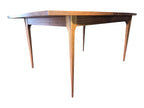Mid Century Modern Broyhill Brasilia walnut dining table in a low front view. Features the Brasilia collection's signature tapered legs and bow-sided rectangle table top. Sold as-is, gently refreshed, including three interior leaves.
