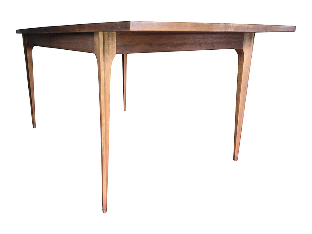 Mid Century Modern Broyhill Brasilia walnut dining table in a low right front view. Features the Brasilia collection's signature tapered legs and bow-sided rectangle table top. Sold as-is, gently refreshed, including three interior leaves.