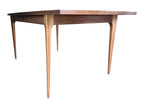 Mid Century Modern Broyhill Brasilia walnut dining table in a low right front view. Features the Brasilia collection's signature tapered legs and bow-sided rectangle table top. Sold as-is, gently refreshed, including three interior leaves.